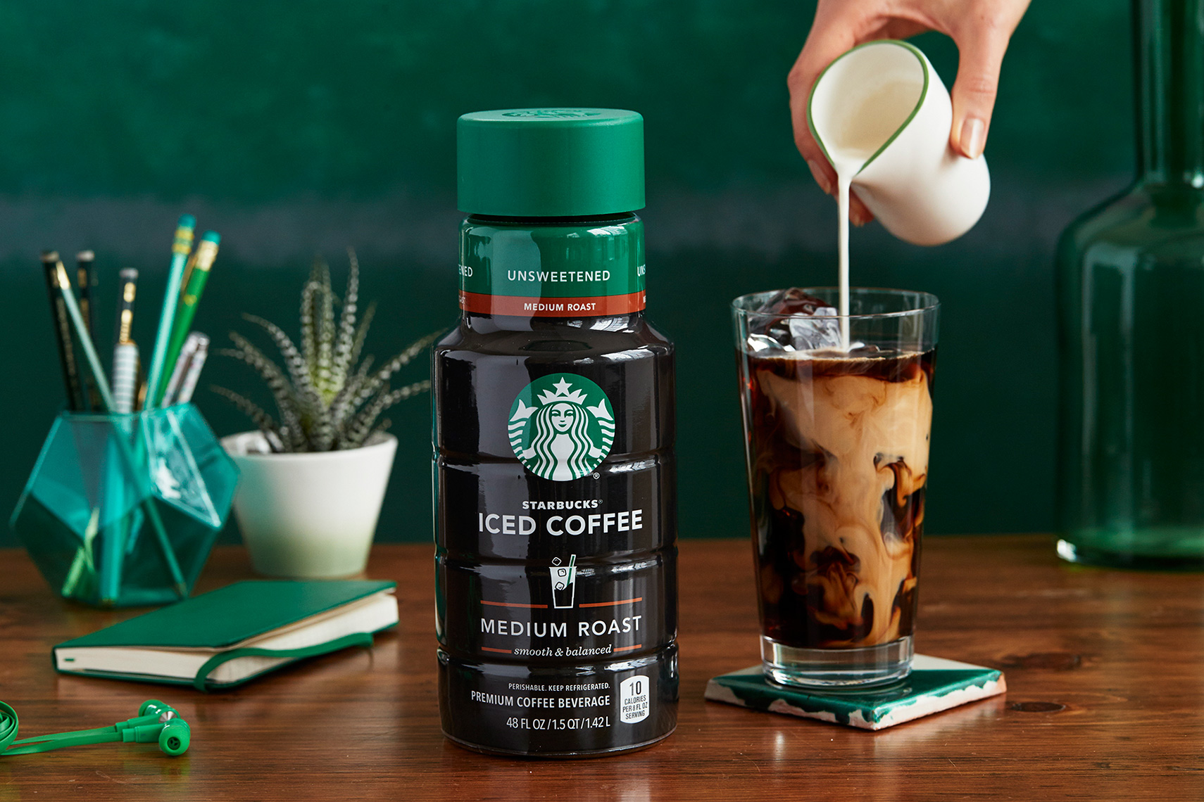Starbucks cold brew coffee bottle with milk being poured into iced coffee glass.