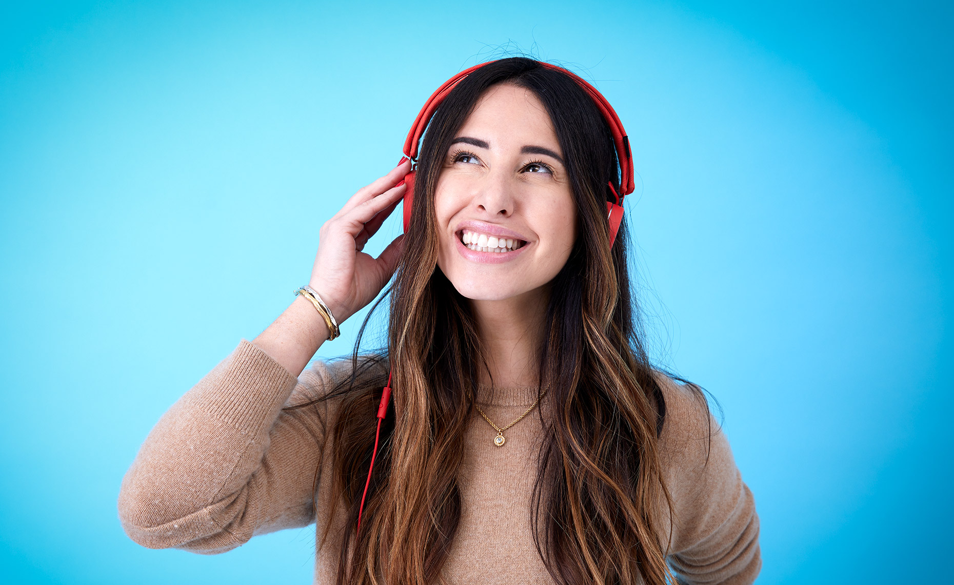 Studio shot of a happy attractive young woman listening to headphones in front of a blue background. Well lit, bright and airy.