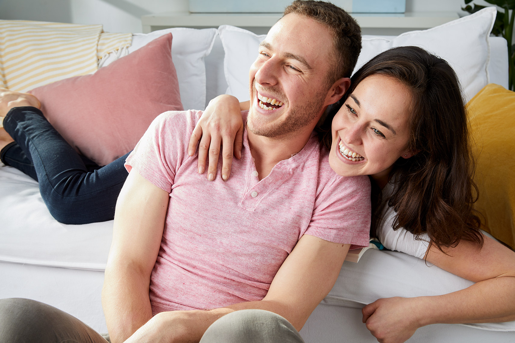 Young man and woman leaning on each other and laughing on the couch.