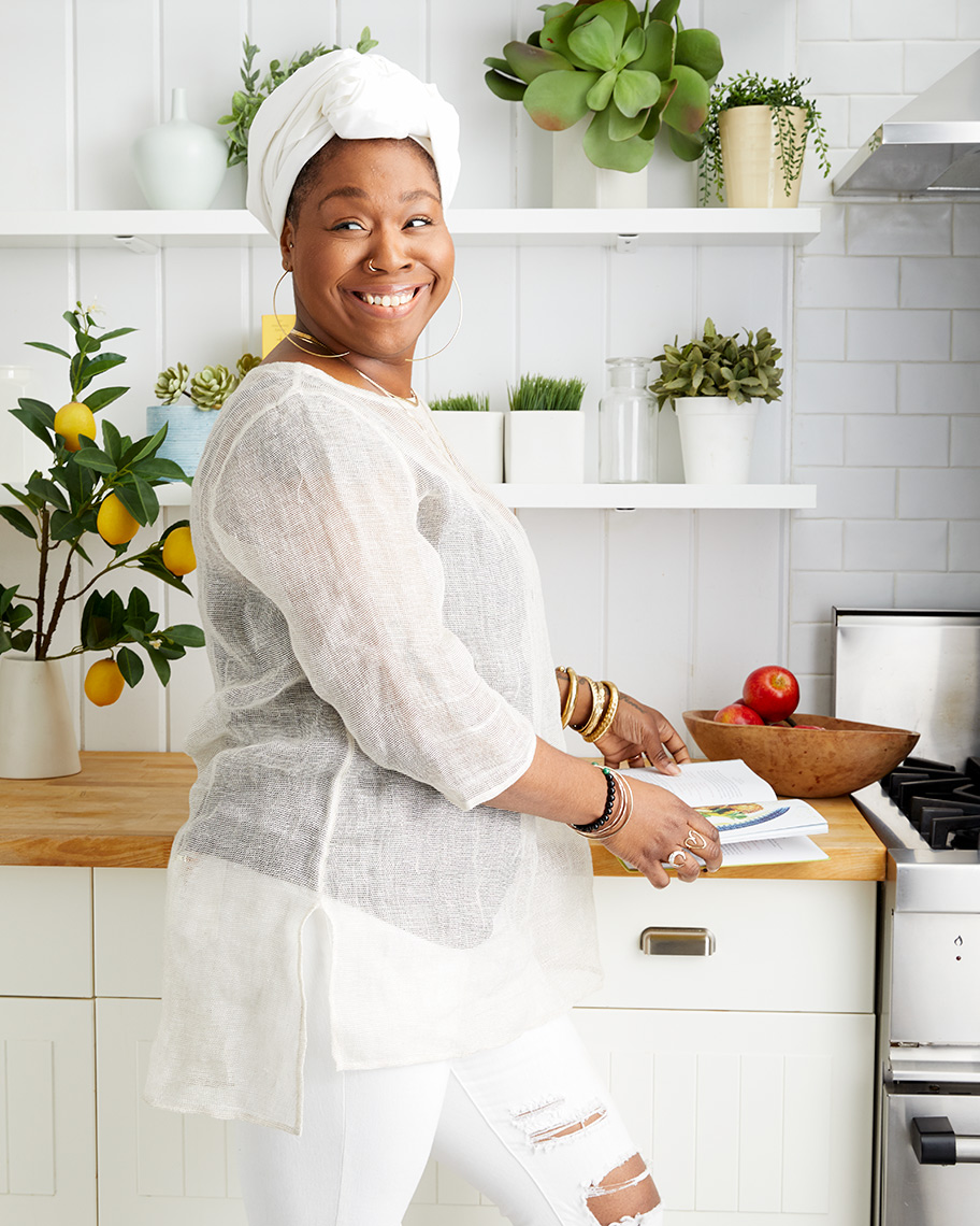 Black African American woman wearing white and smiling in a bright modern kitchen interior.