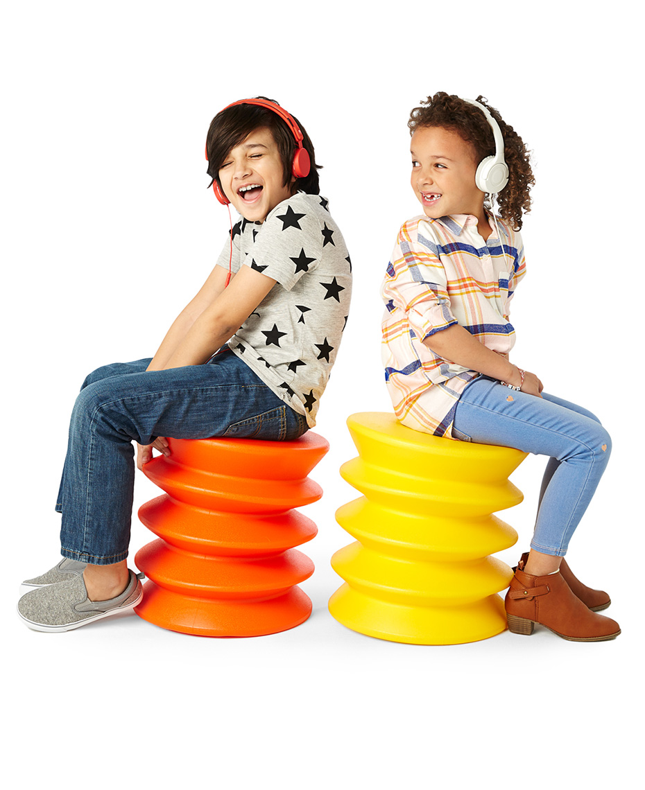 Two mixed race kids sitting on brightly colored stools, shot on white background.