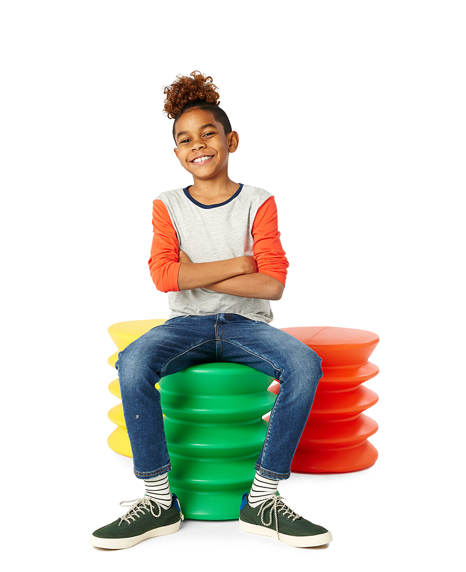 African American boy smiling and  sitting on a colorful stool.