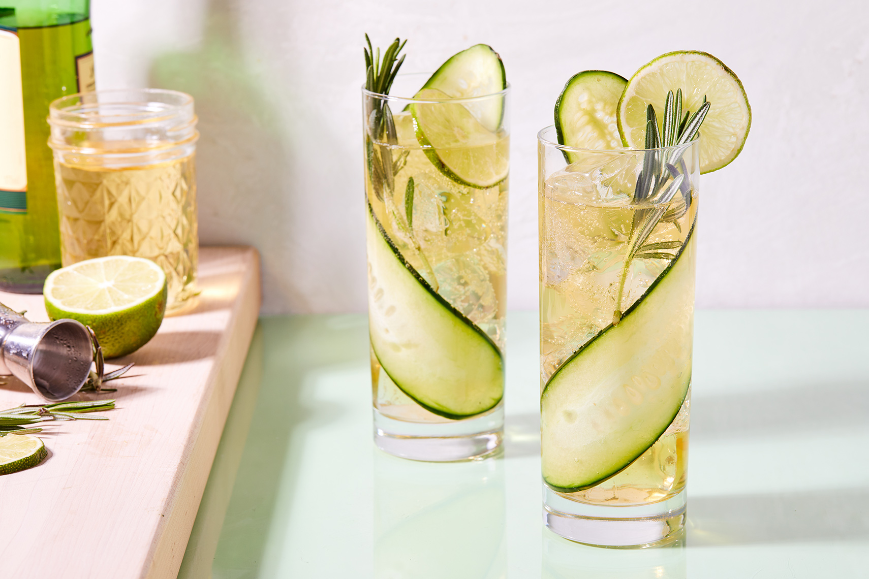 Two Whiskey Tonics with cucumber garnish and pale green modern styling shot in clean daylight for Delish.